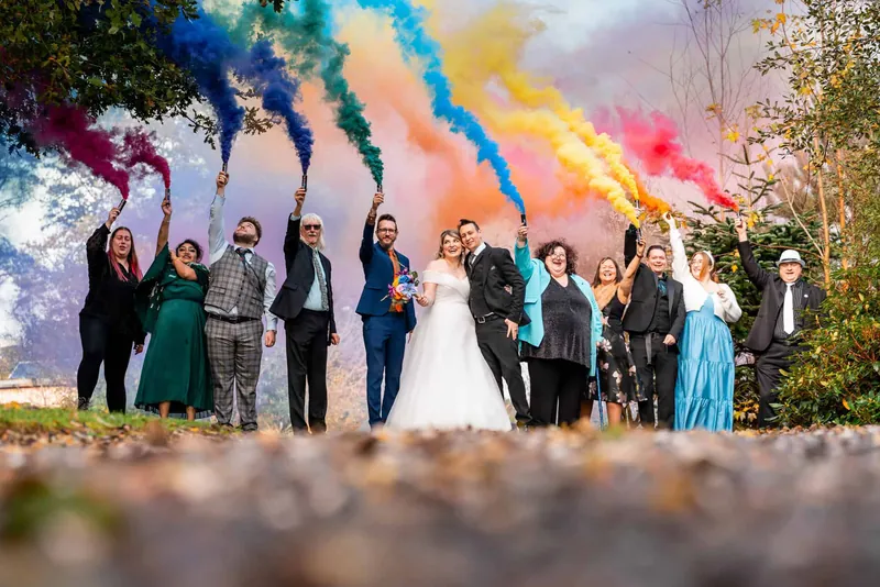 Wedding party holding rainbow smoke bombs in the grounds at Tree Top Escape