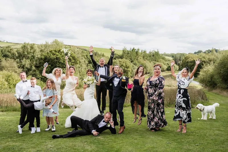 Bride, groom and guests jumping for joy in the grounds at Tree Top Escape, with their dog